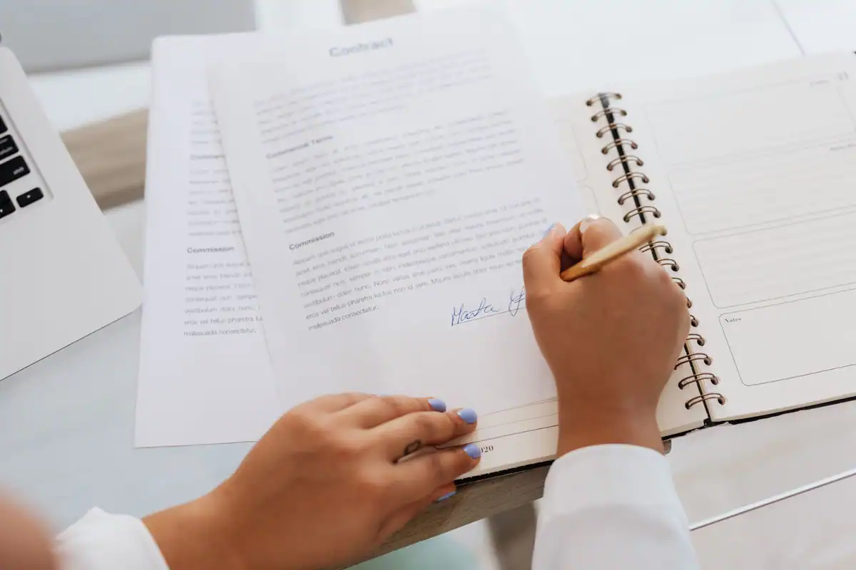 Mâini care semnează un document oficial pe un birou, simbol al angajamentelor climatice