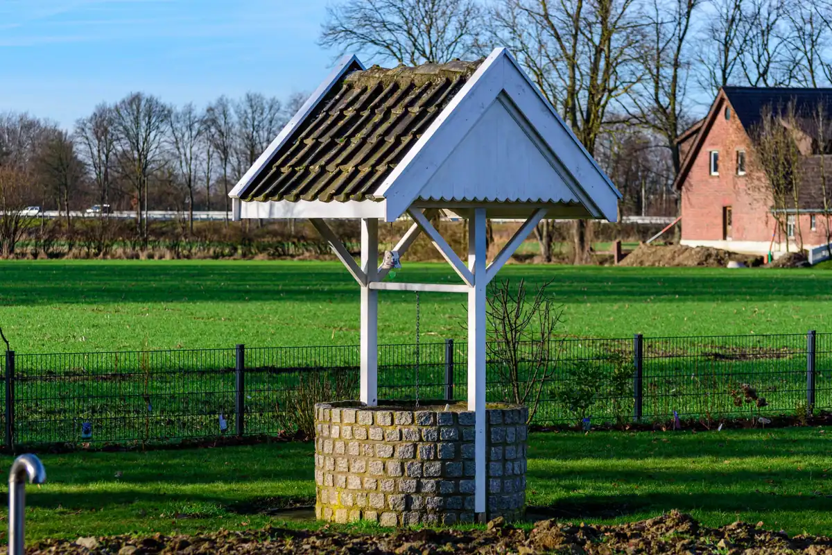 Fântână veche din piatră cu acoperiș de lemn într-un peisaj rural liniștit