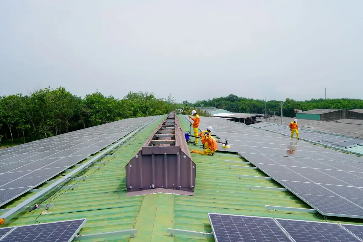 Echipă care montează panouri fotovoltaice pe un acoperiș mare, sub cer senin
