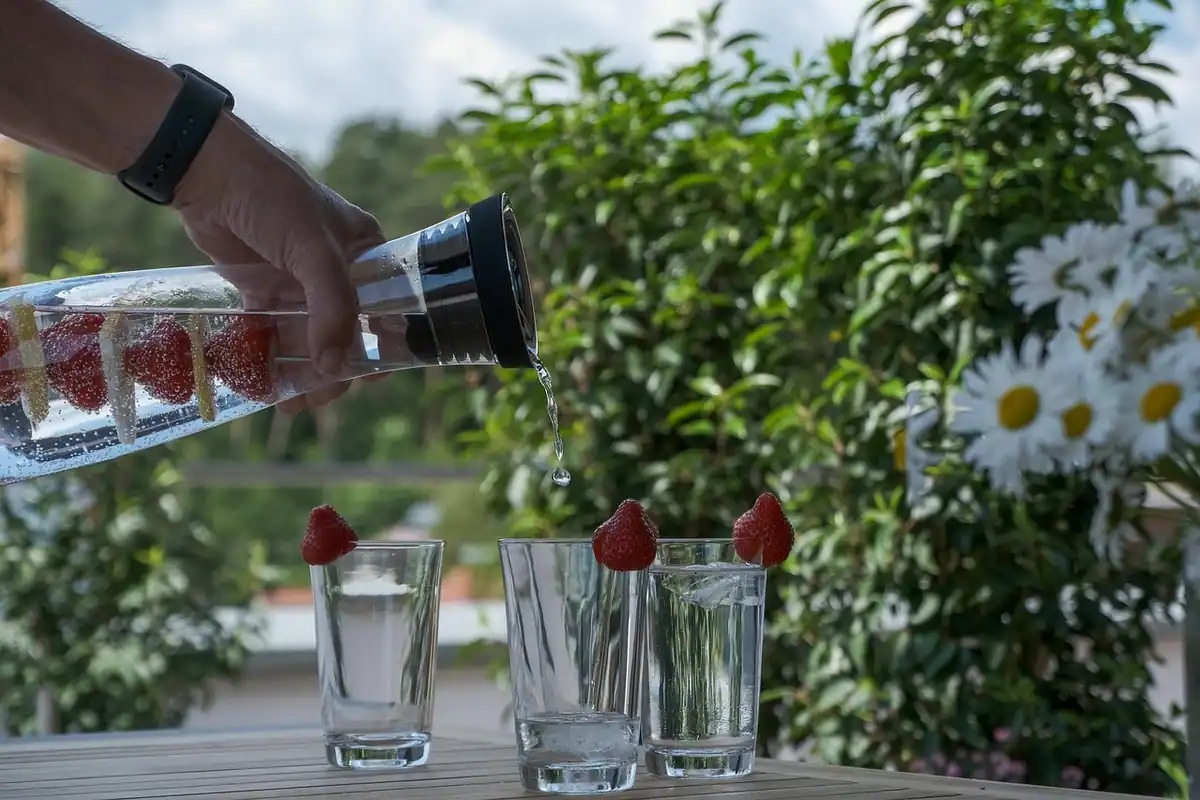 Apă filtrată turnată dintr-o carafă de sticlă în pahare, pe o masă în grădină