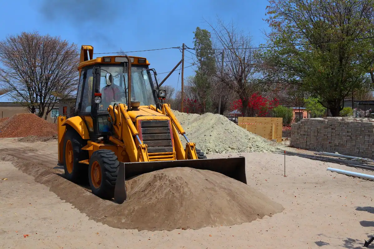 Buldoexcavator galben care sapă pământul pe un șantier, pentru montarea unui bazin