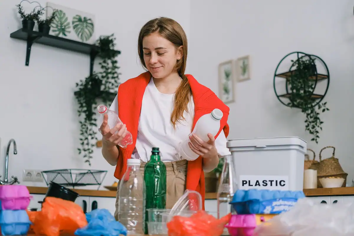 Femeie zâmbitoare care sortează sticle de plastic în bucătărie pentru reciclare