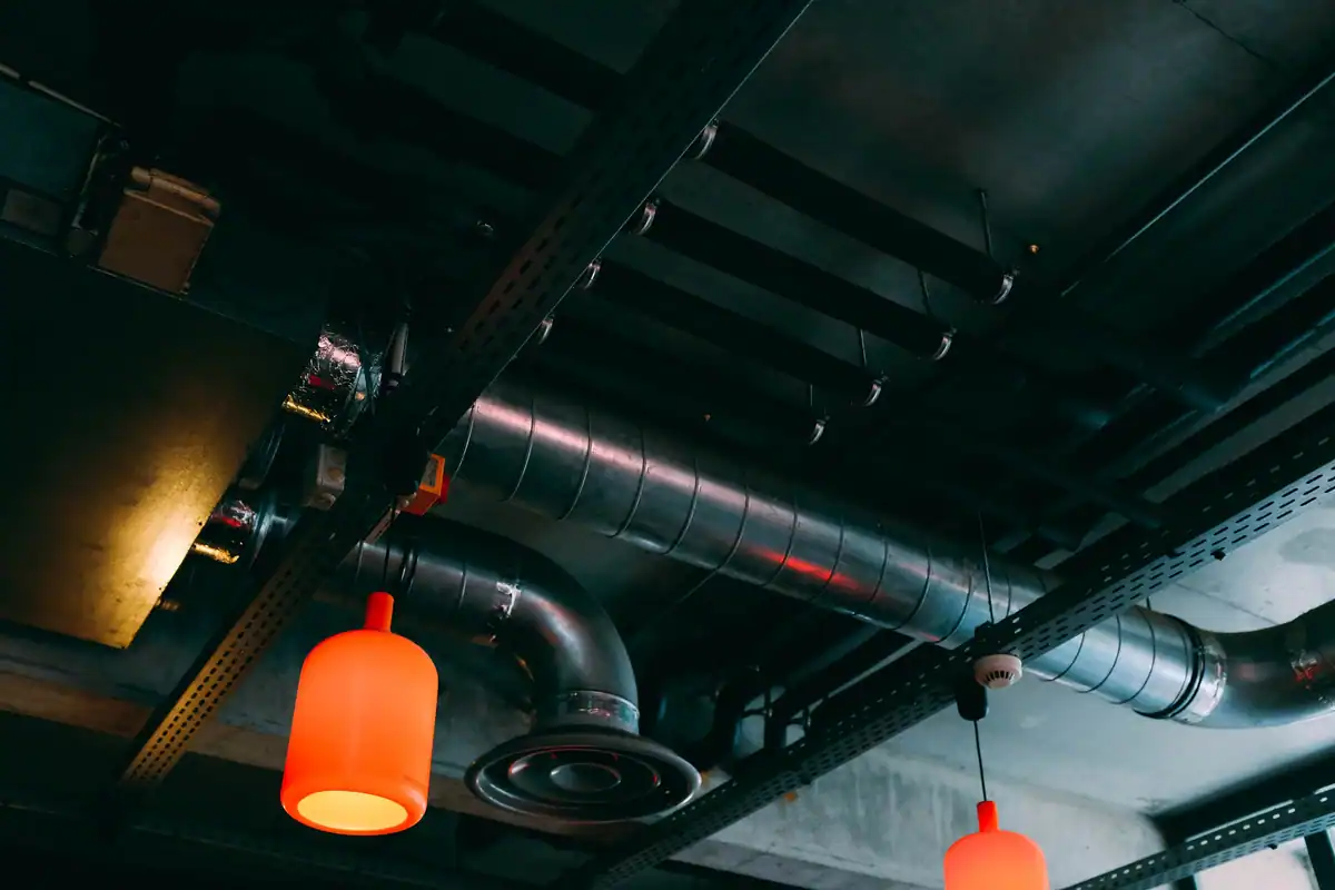 Tavan industrial modern cu tubulatură de ventilație și lămpi roșii, văzut de jos